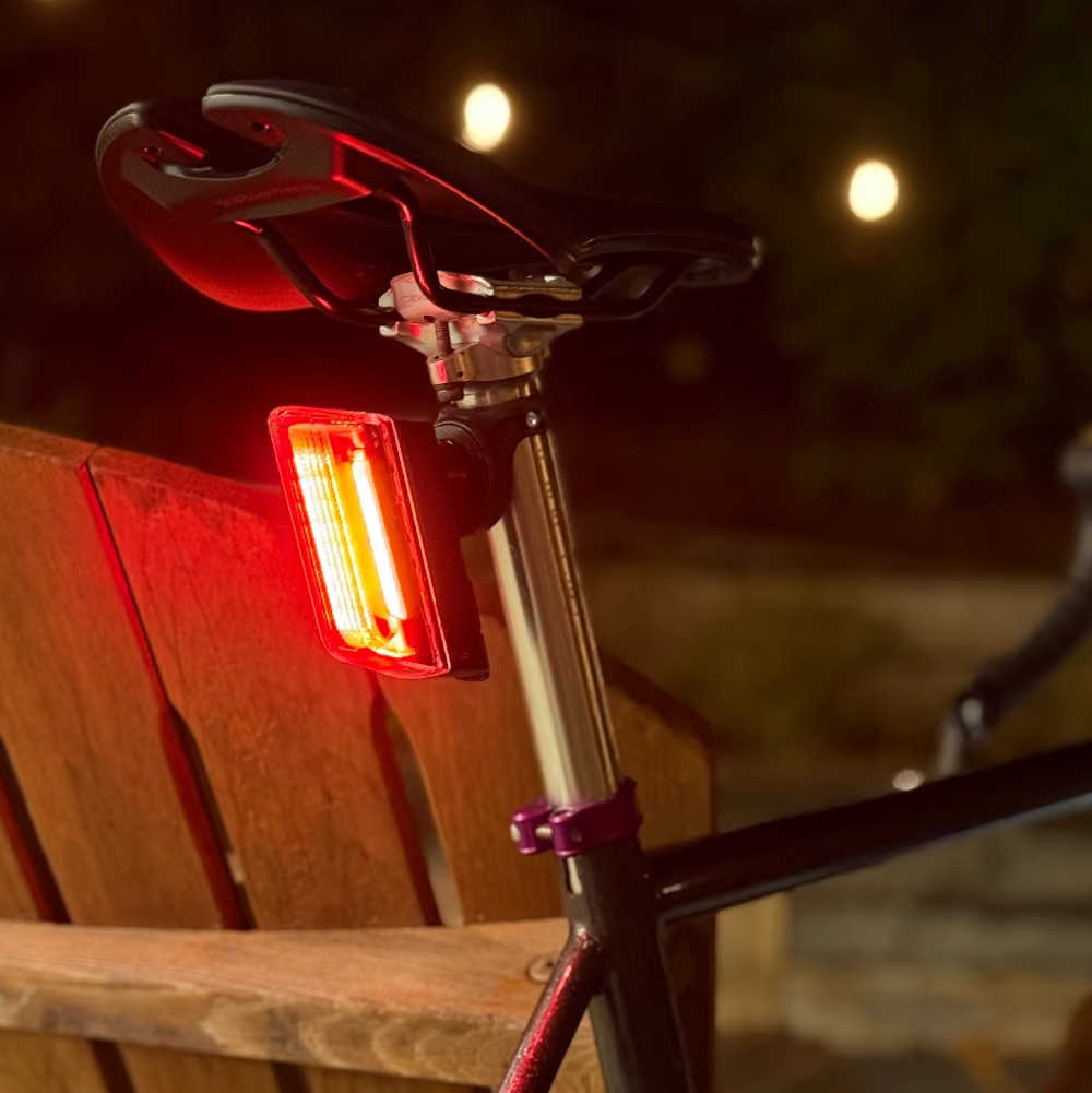 Bicycle with a red tail light attached, parked on a wooden chair outdoors.