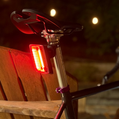 Bicycle with a red tail light attached, parked on a wooden chair outdoors.