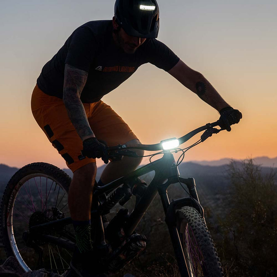 Mountain biker riding at sunset with the Trail Evo handlebar light and Hangover helmet light switched on